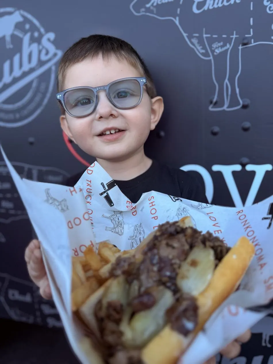 A young guest holding a cheesesteak and fries in Chubs paper