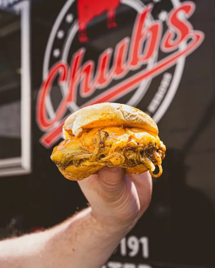 Double smash burger with melted cheese held in front of the Chubs truck logo